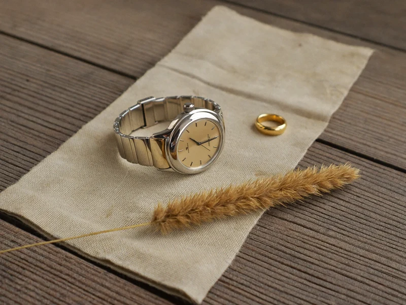 Montre et bague posées sur du lin brut près d'une herbe sèche