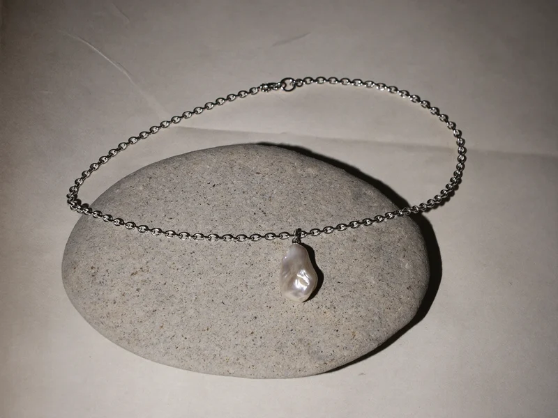 Collier d'argent à perle irrégulière drapé sur un galet
